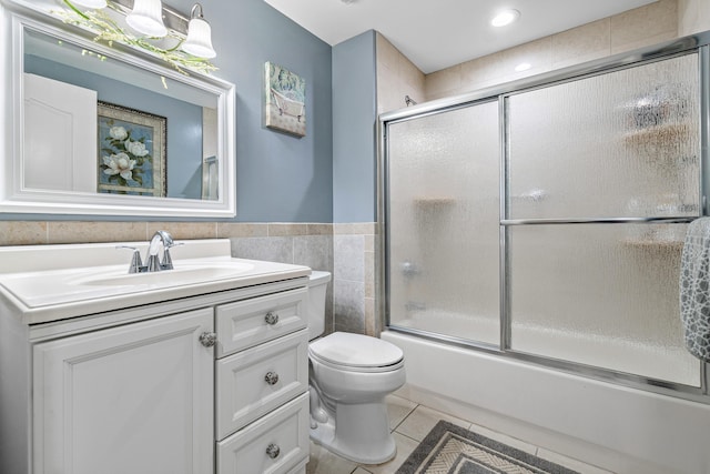 full bath featuring tile patterned flooring, toilet, bath / shower combo with glass door, vanity, and tile walls