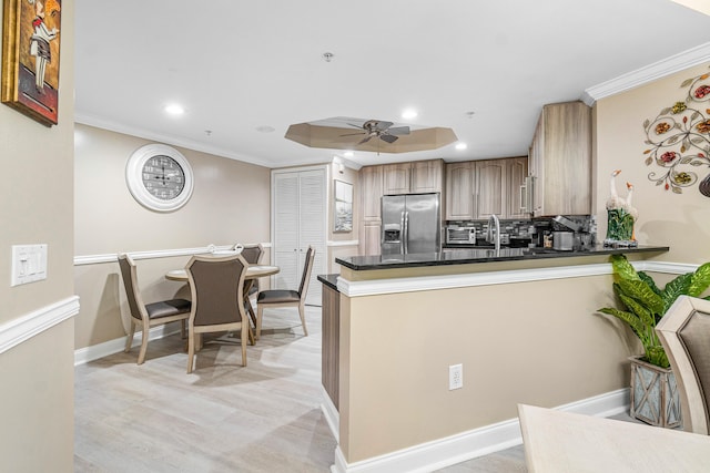 kitchen featuring crown molding, stainless steel refrigerator with ice dispenser, dark countertops, backsplash, and a ceiling fan