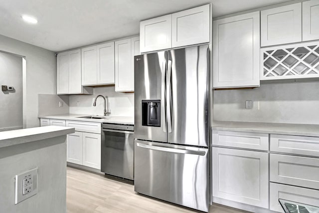 kitchen with sink, tasteful backsplash, stainless steel appliances, light hardwood / wood-style floors, and white cabinets