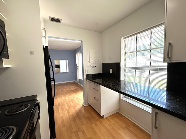 kitchen featuring dark stone countertops, light hardwood / wood-style floors, black fridge, white cabinets, and stove