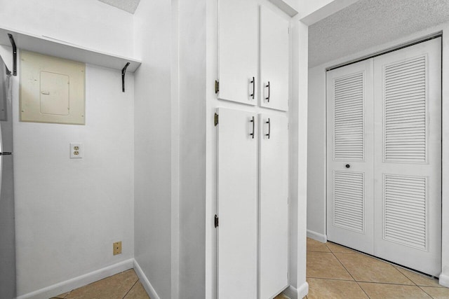 interior space featuring light tile patterned floors, electric panel, baseboards, and a textured ceiling