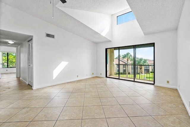 empty room with light tile patterned floors, high vaulted ceiling, a textured ceiling, and a healthy amount of sunlight