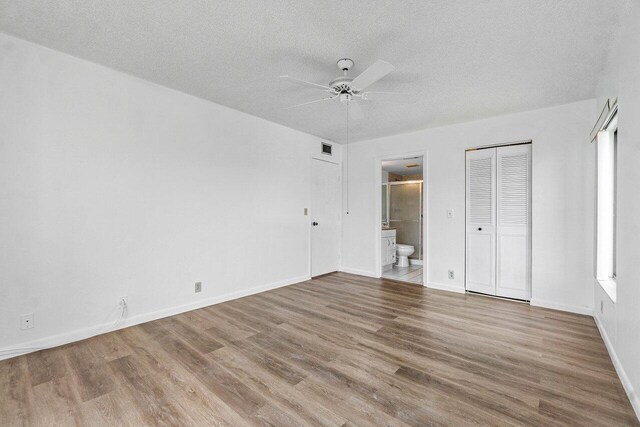 unfurnished bedroom featuring a textured ceiling, ensuite bath, a closet, ceiling fan, and wood-type flooring