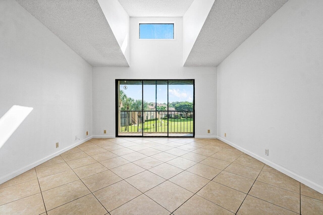 spare room with light tile patterned floors, a high ceiling, a textured ceiling, and baseboards