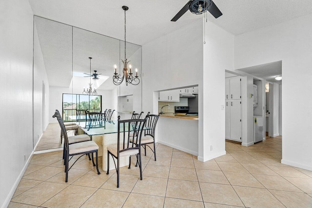 tiled dining space with ceiling fan with notable chandelier, a textured ceiling, sink, and high vaulted ceiling