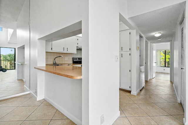 kitchen with stove, a textured ceiling, light tile patterned floors, white cabinets, and backsplash