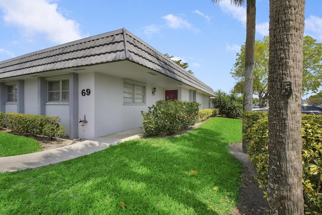 view of home's exterior featuring a tile roof, mansard roof, a lawn, and stucco siding