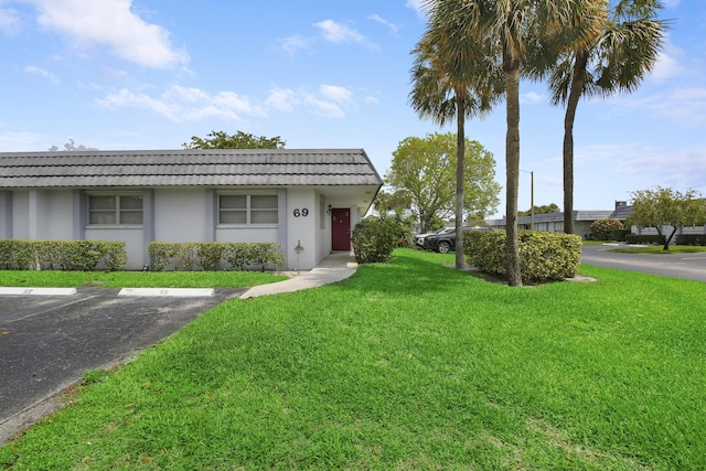 view of front of property with stucco siding, uncovered parking, a front lawn, and a tiled roof