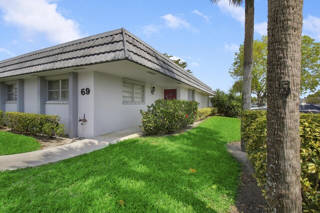 view of home's exterior featuring stucco siding, mansard roof, and a yard