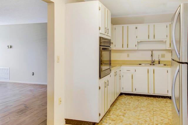 kitchen featuring white cabinetry, sink, oven, white fridge, and light hardwood / wood-style floors