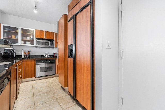 kitchen with appliances with stainless steel finishes, sink, dark stone counters, light tile patterned floors, and track lighting