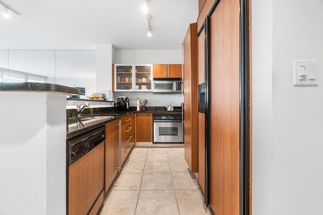 kitchen with rail lighting, sink, light tile patterned floors, dark stone countertops, and stainless steel appliances