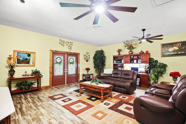 living room featuring ceiling fan, light hardwood / wood-style flooring, and a textured ceiling