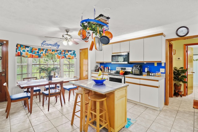 kitchen with ceiling fan, a kitchen bar, white cabinetry, a center island, and range with electric stovetop