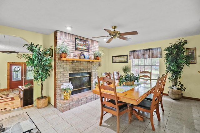 tiled dining room with a ceiling fan, a brick fireplace, plenty of natural light, and baseboards