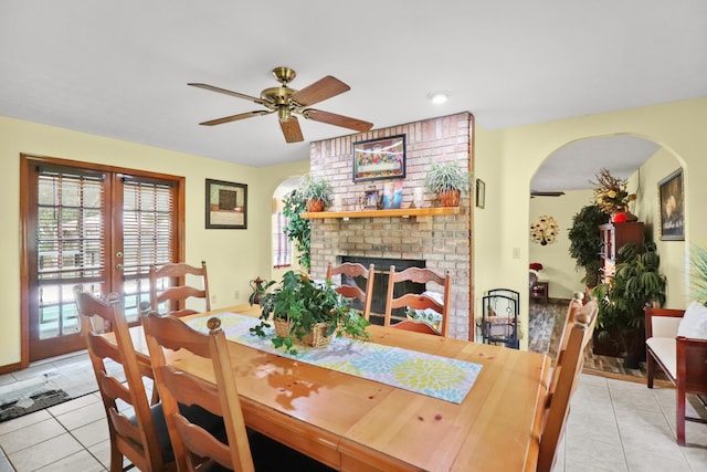 dining room with arched walkways, light tile patterned flooring, a ceiling fan, french doors, and a brick fireplace