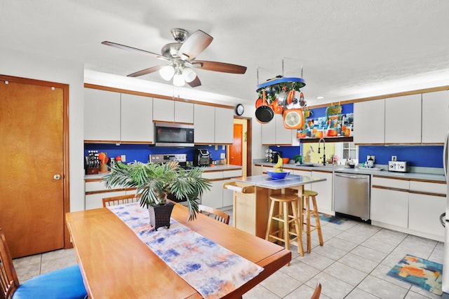 kitchen featuring light tile patterned floors, a breakfast bar area, stainless steel appliances, a kitchen island, and white cabinetry