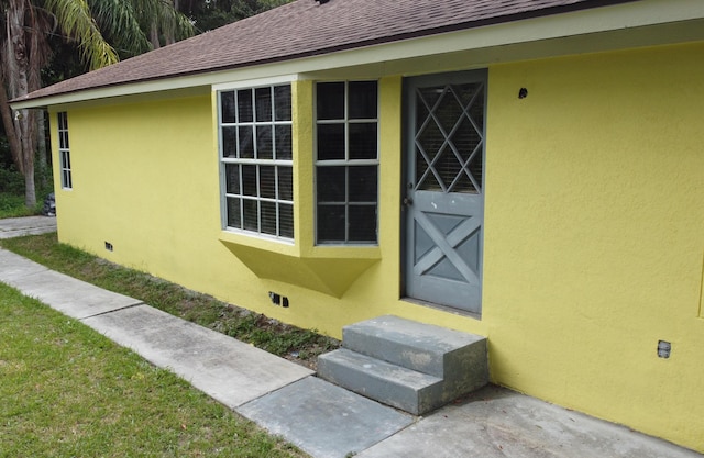 property entrance with crawl space, roof with shingles, and stucco siding