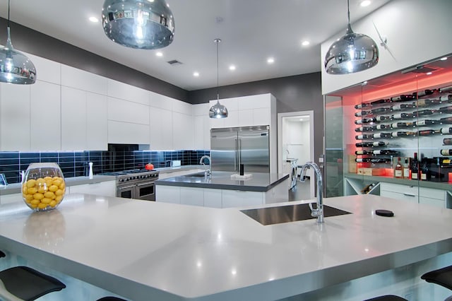 kitchen with pendant lighting, a kitchen island with sink, sink, premium appliances, and white cabinetry