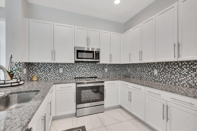 kitchen featuring decorative backsplash, stainless steel appliances, light stone counters, light tile patterned floors, and white cabinets