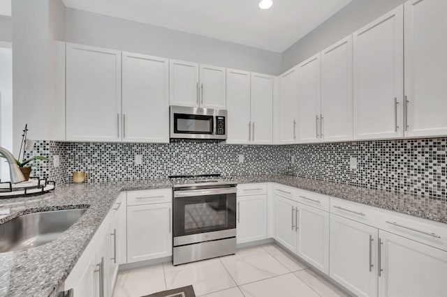 kitchen with sink, white cabinetry, light stone counters, appliances with stainless steel finishes, and backsplash