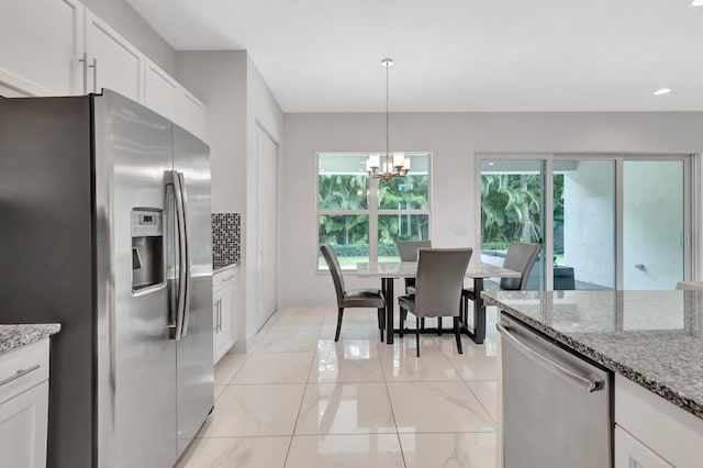 kitchen with stainless steel appliances, white cabinetry, pendant lighting, and light stone counters