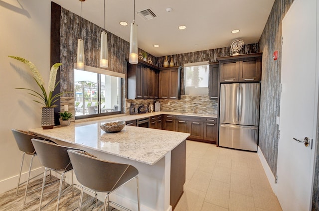 kitchen with stainless steel fridge, kitchen peninsula, plenty of natural light, and hanging light fixtures