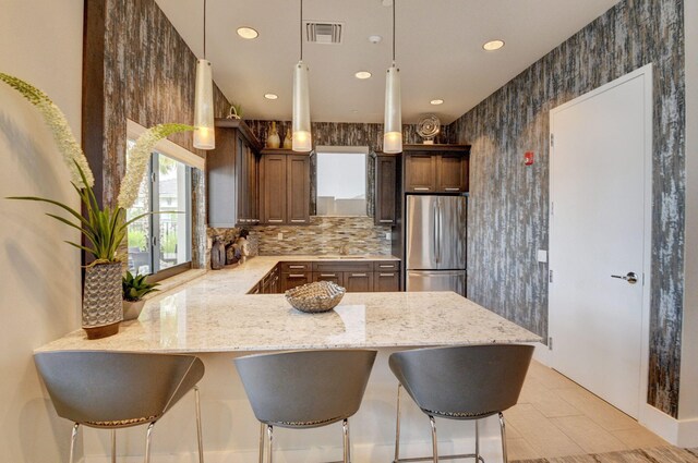 kitchen with light stone counters, kitchen peninsula, stainless steel refrigerator, pendant lighting, and sink