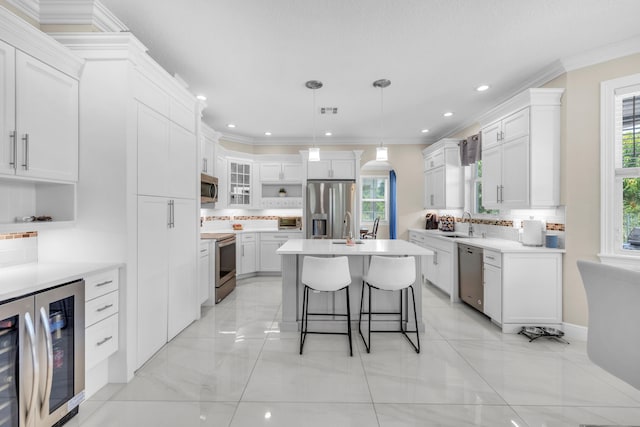 kitchen featuring appliances with stainless steel finishes, wine cooler, crown molding, a kitchen island, and hanging light fixtures