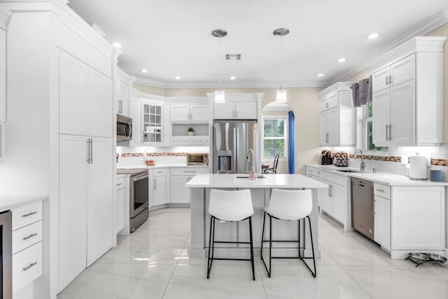 kitchen with appliances with stainless steel finishes, decorative backsplash, a kitchen island, light tile patterned floors, and pendant lighting