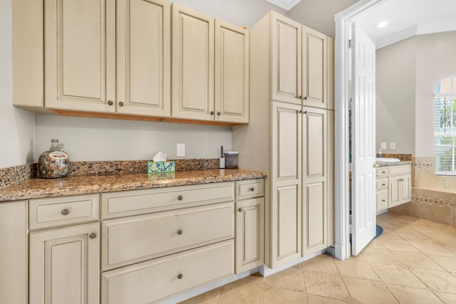 kitchen featuring light tile patterned flooring, cream cabinetry, ornamental molding, and stone counters