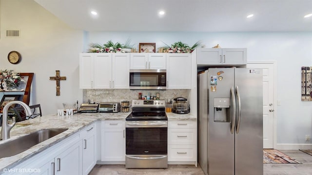 kitchen featuring visible vents, decorative backsplash, appliances with stainless steel finishes, white cabinetry, and a sink