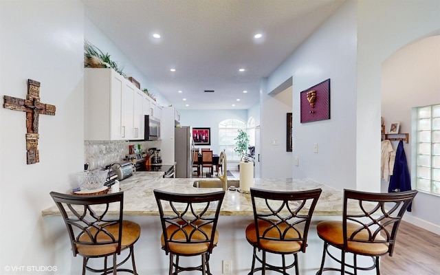 kitchen with a breakfast bar, stainless steel appliances, white cabinetry, a sink, and a peninsula