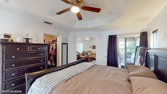 bedroom featuring a walk in closet, a closet, visible vents, ceiling fan, and a textured ceiling