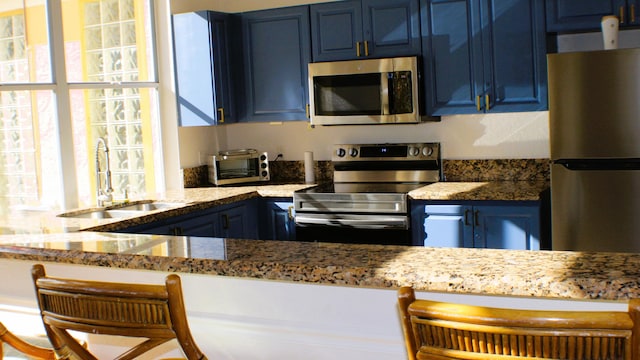 kitchen with a breakfast bar area, stone countertops, blue cabinets, stainless steel appliances, and a sink