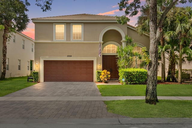 mediterranean / spanish house with decorative driveway, stucco siding, a front yard, a garage, and a tiled roof