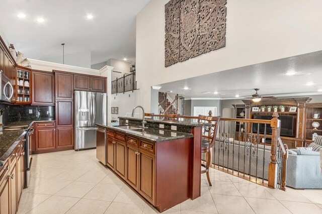 kitchen with stainless steel appliances, sink, a high ceiling, dark stone counters, and ceiling fan