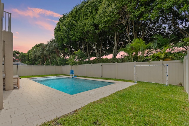 pool at dusk with a patio area and a lawn