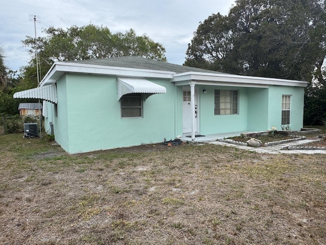 view of front facade featuring stucco siding, central air condition unit, and a front yard