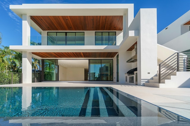 back of house with an outdoor pool, a balcony, stairway, and a patio