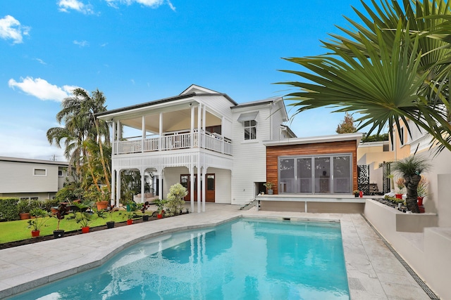 back of property with a balcony, an outdoor pool, and a patio area