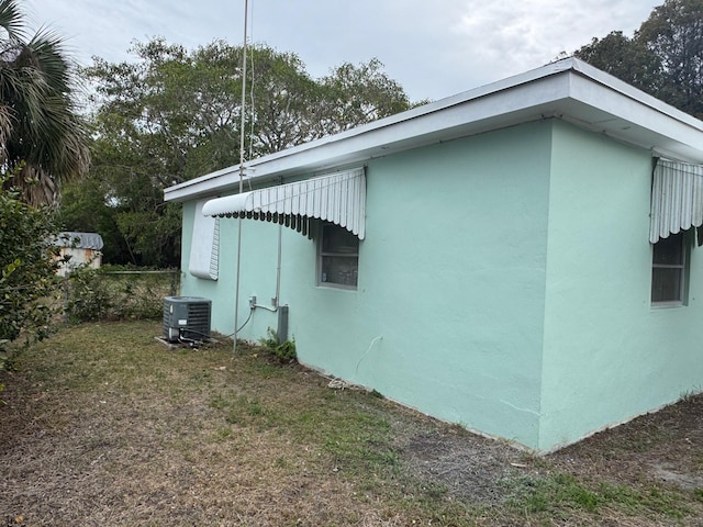 view of side of property with central air condition unit, stucco siding, and fence