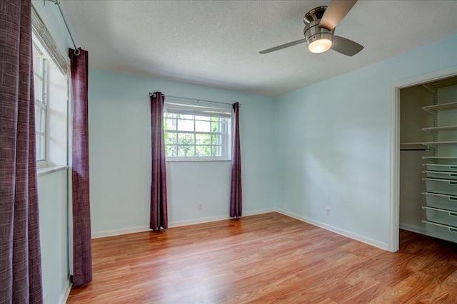 unfurnished bedroom featuring a walk in closet, ceiling fan, light hardwood / wood-style floors, a textured ceiling, and a closet