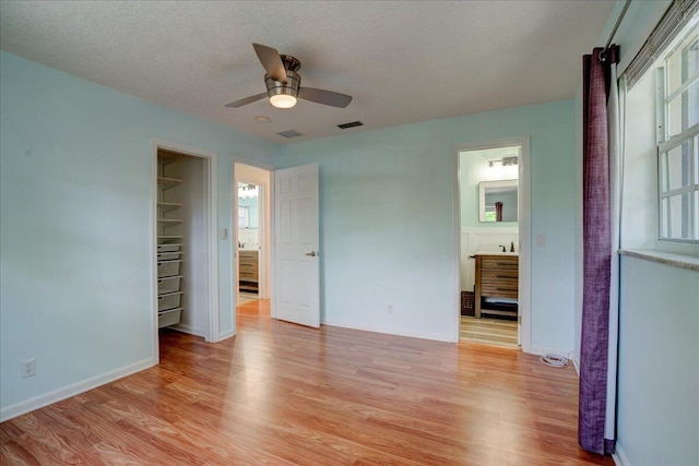 unfurnished bedroom featuring ensuite bath, ceiling fan, light hardwood / wood-style floors, a textured ceiling, and a closet