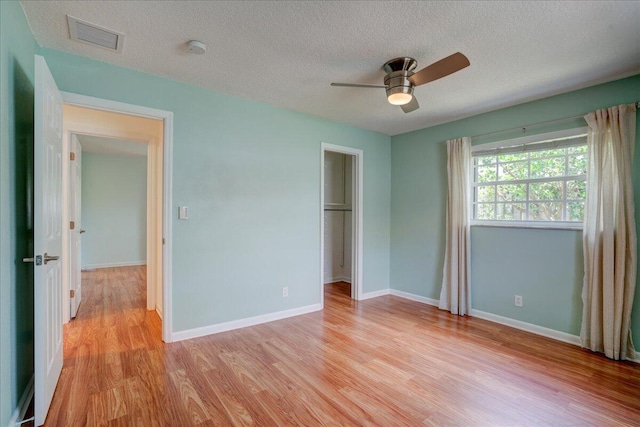 unfurnished bedroom with ceiling fan, a textured ceiling, a walk in closet, a closet, and light wood-type flooring