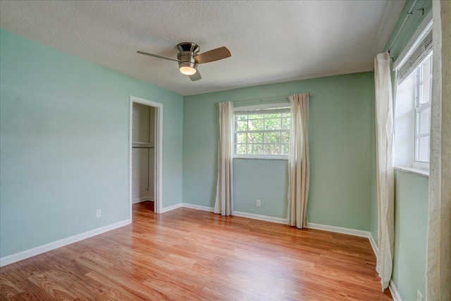 unfurnished bedroom with ceiling fan, a spacious closet, a textured ceiling, and light wood-type flooring