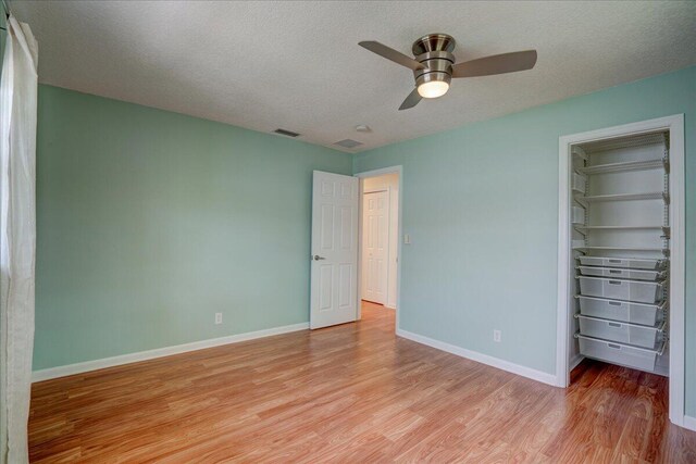 unfurnished bedroom featuring a walk in closet, light hardwood / wood-style floors, a closet, and a textured ceiling