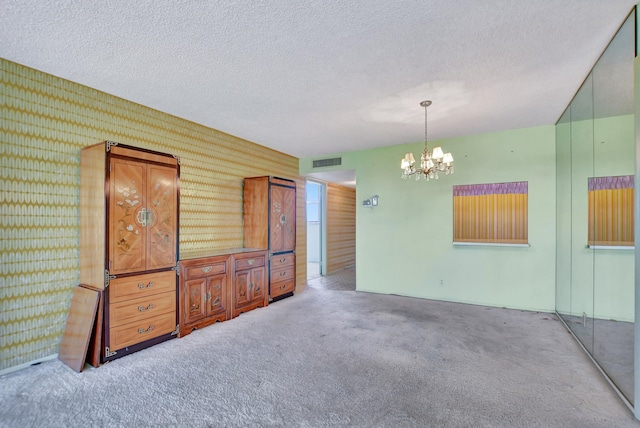 spare room with a textured ceiling, carpet floors, and a chandelier