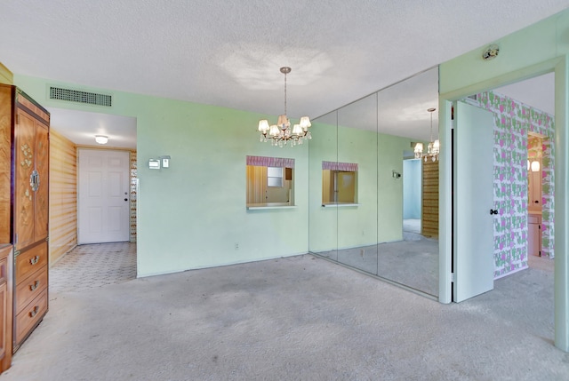 carpeted spare room featuring a textured ceiling and a chandelier