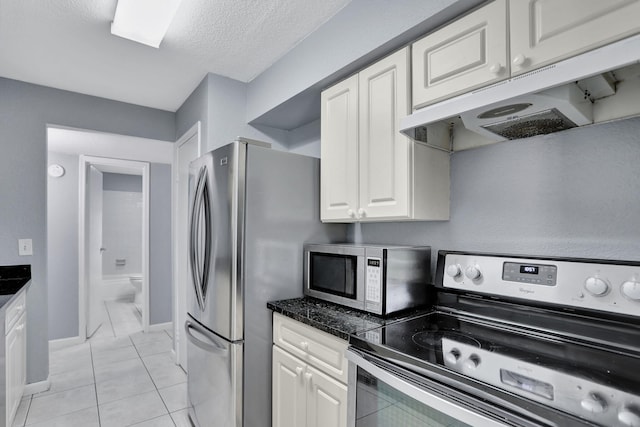 kitchen with a textured ceiling, appliances with stainless steel finishes, white cabinetry, and light tile patterned flooring